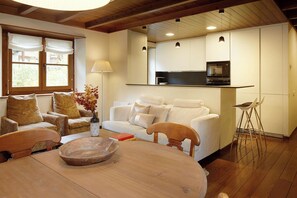 Un salon chaleureux avec une table à manger en bois, un ensemble de canapés et un coin cuisine équipé d’un téléviseur et d’appareils électroménagers modernes.