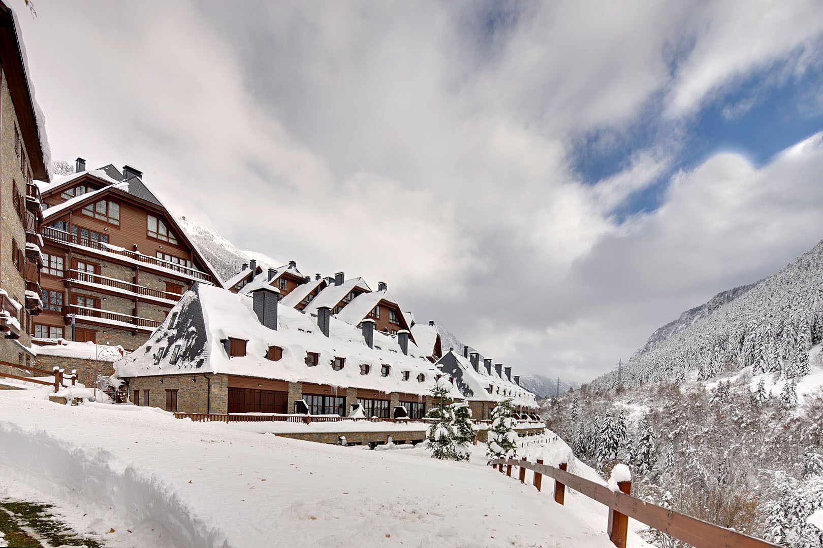 A snow-covered lodge with multiple buildings, wooden balconies, and a mountainous backdrop.