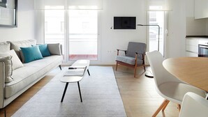 A modern living room with a sofa, a coffee table, a dining table, and a chair. There is a TV mounted on the wall and a window with a view of the outside. - San Francisco 2 by FeelFree Rentals (Donostia)