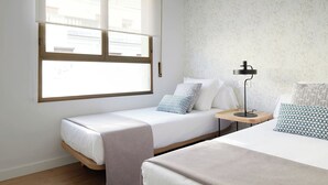 A room with two beds, a window with blinds, a bedside table with a lamp, and a patterned wallpaper. - San Francisco 2 by FeelFree Rentals (Donostia)