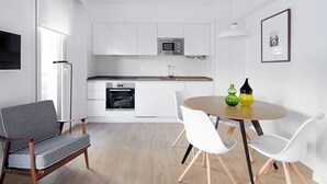 A modern kitchen with white cabinetry, a built-in oven, and a microwave. There is a dining area with a round table and white chairs. - San Francisco 2 by FeelFree Rentals (Donostia)