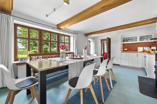 A modern kitchen with white cabinets, wooden beams, and a dining area with a table and chairs. - Vacation apartment in the country house "Hohe Luft" with large garden and 1500m to the Baltic Sea (Steinberg)
