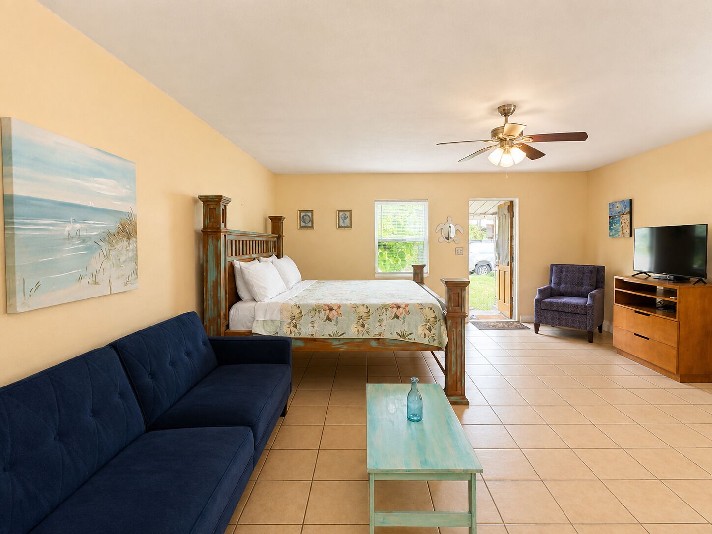 A bedroom with a bed, a sofa, a television, and a ceiling fan.
