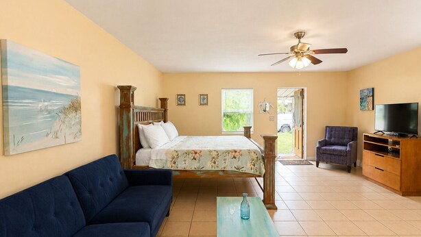 A bedroom with a bed, a sofa, a television, and a ceiling fan. - Cozy Gulfport Studio with King Bed + Full Kitchen walkable to Beach Blvd (Gulfport)