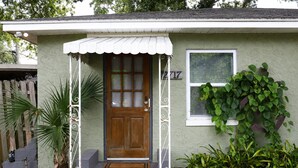A single-story house with a front porch, a wooden door, and a window with blinds. - Cozy Gulfport Studio with King Bed + Full Kitchen walkable to Beach Blvd (Gulfport)