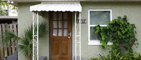 Een gelijkvloers huis met een veranda, een houten deur en een raam met zonwering.