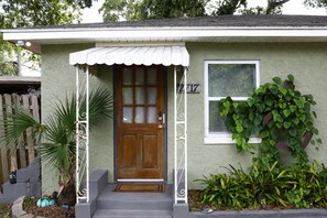 A single-story house with a front porch, a wooden door, and a window with blinds. - Cozy Gulfport Studio with King Bed + Full Kitchen walkable to Beach Blvd (Gulfport)