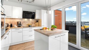 Een moderne keuken met witte kastjes, een houten aanrecht en een stadszicht door grote schuifdeuren.
