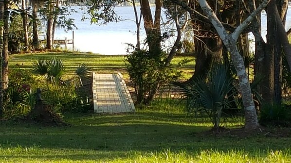 A pathway leading to a body of water, surrounded by lush greenery and trees. - Charming, historic riverfront lodge on 7 wooded acres, 6 bedrooms, mini split (Mobile)