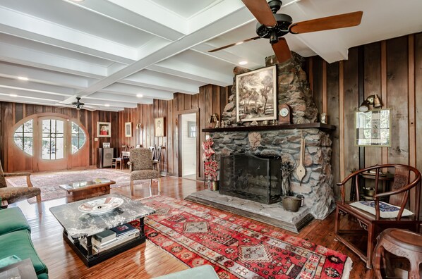 A spacious living room with a stone fireplace, wooden walls, and a large window.