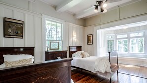 Une chambre à coucher avec un lit en bois, une table de chevet, une commode et une fenêtre donnant sur des arbres.