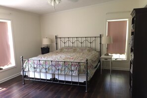 Un dormitorio con estructura de cama de metal, cubrecama floral, dos lámparas de noche, mesita de noche y un armario.