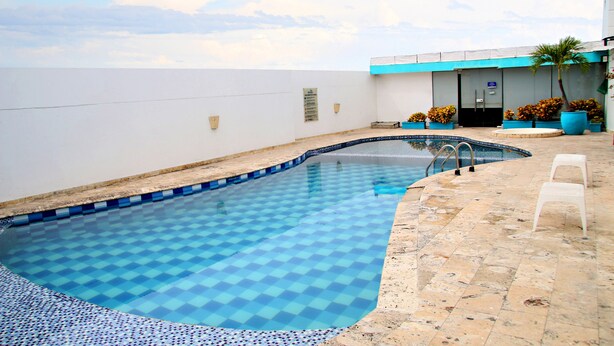 Ein Pool mit Schachbrettmuster, umgeben von einer Fliesenveranda und einem Gebäude mit blauer Akzentwand.