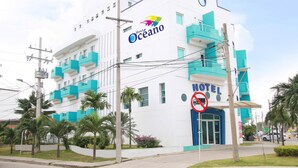 Ein weißes Gebäude mit türkisblauen Akzenten, mit dem Schriftzug "Hotel Oceano", das Balkone und eine blaue Eingangstür zeigt.