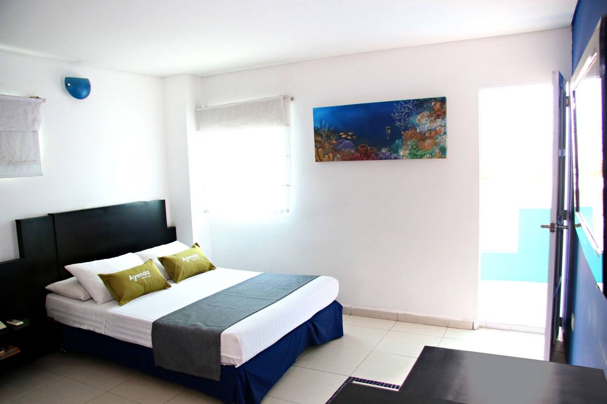 Habitación de hotel con cama, mesita de noche, un cuadro y ventana.