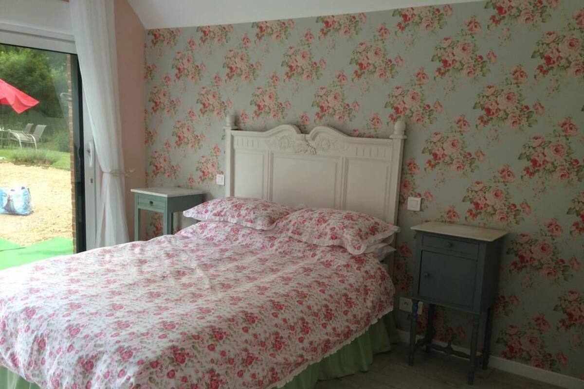 Ein Schlafzimmer mit floraler Tapete, einem weißen Bett mit grünem Bettvorhang und einem kleinen Nachttisch.