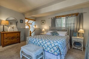A bedroom with a bed, a dresser, a chair, a window with curtains, and a bedside table with a lamp. - L'Auberge Des Oiseaux Chantants (Willeman)