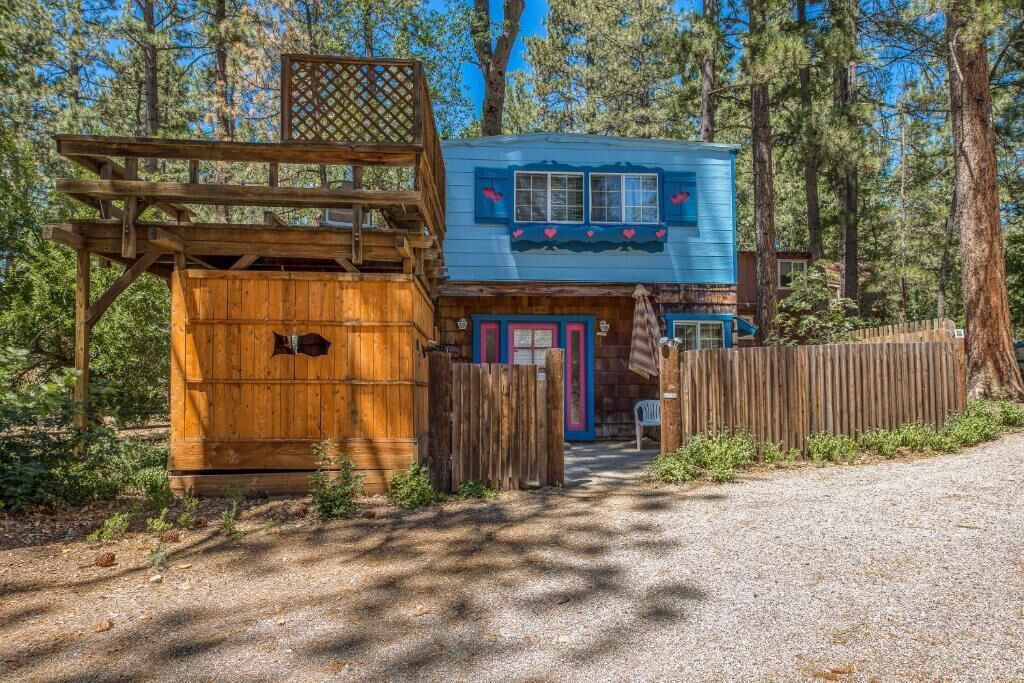 A rustic cabin with a wooden deck, a blue exterior, and a fenced yard.