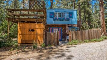 A rustic cabin with a wooden deck, a blue exterior, and a fenced yard.