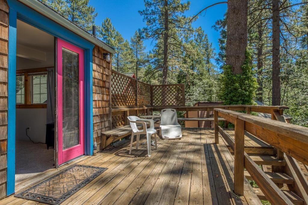 Une terrasse en bois avec une clôture en bois, une porte dotée d’un cadre rose et deux chaises en plastique blanches.