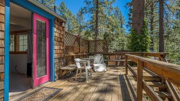 Une terrasse en bois avec une clôture en bois, une porte dotée d’un cadre rose et deux chaises en plastique blanches.