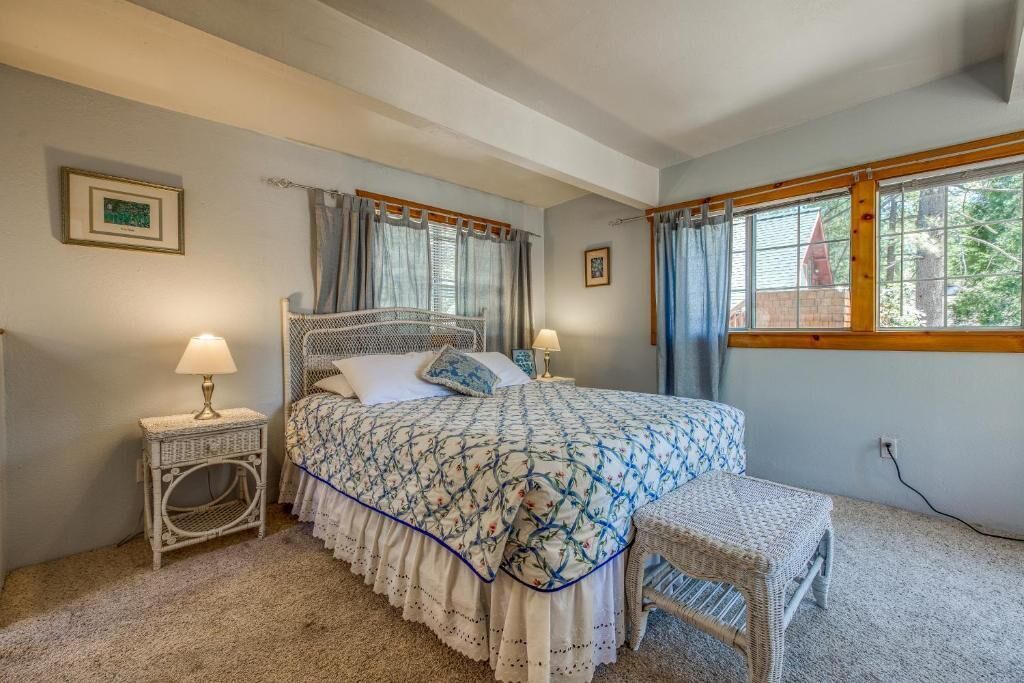 A bedroom with a bed, two bedside tables, a bench, and a window with curtains.