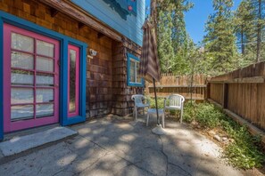 A wooden house with a pink door and blue trim, a patio with two white plastic chairs, and a wooden fence. - L'Auberge Des Oiseaux Chantants (Willeman)
