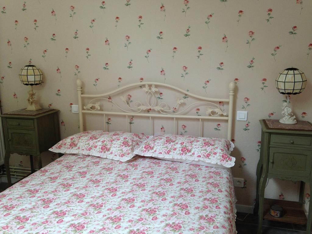 A bedroom with a floral-patterned bedspread, a white ornate headboard, two bedside tables with lamps, and a green nightstand.