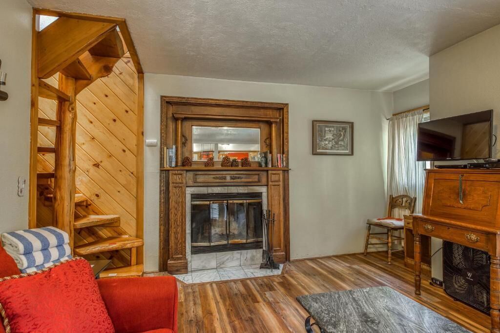 A living room with a fireplace, wooden staircase, and a television.