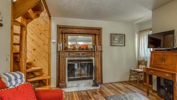 A living room with a fireplace, wooden staircase, and a television.
