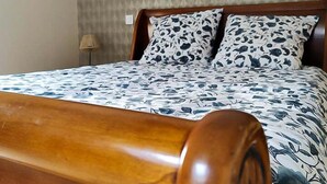 A bed with a wooden frame and floral bedding in a room with a patterned wall and a lamp. - L'Auberge Des Oiseaux Chantants (Willeman)