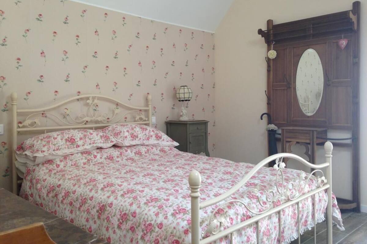 Ein Schlafzimmer mit einem blumengemusterten Bettbezug, einem Holzkopfstück, einem Nachttisch mit Lampe und einem Spiegel an der Wand.