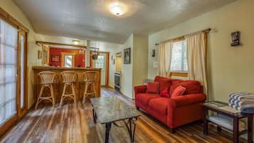 Una sala acogedora con un sofá rojo, piso de madera y un comedor con sillas de mimbre.