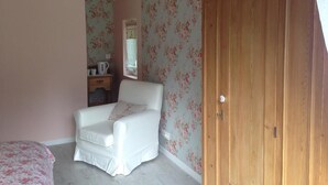 A bedroom with a bed, a white chair, a wooden wardrobe, and floral wallpaper. - L'Auberge Des Oiseaux Chantants (Willeman)