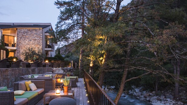 A wooden deck with outdoor seating, a stone wall, and a view of a river.