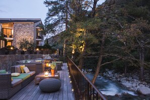 A wooden deck with outdoor seating, a stone wall, and a view of a river.