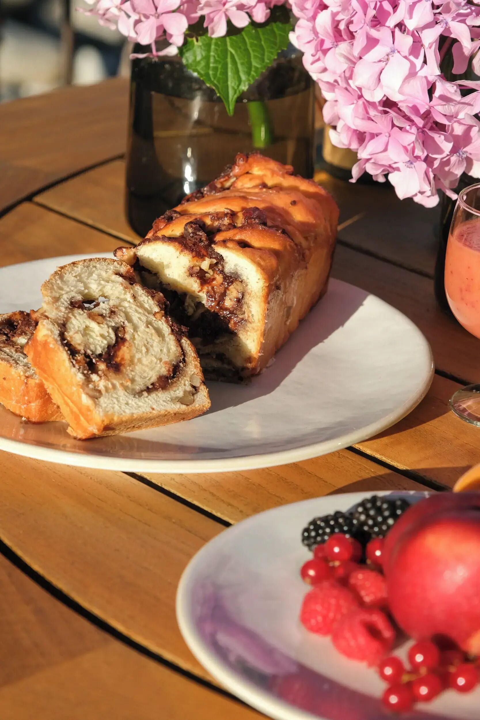 Una porción de rollo de canela en un plato blanco, un rollo de canela entero y un plato con frutos rojos.