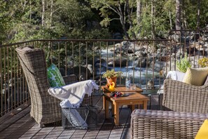 A deck with wicker furniture, a table with a potted plant, and a view of a river.