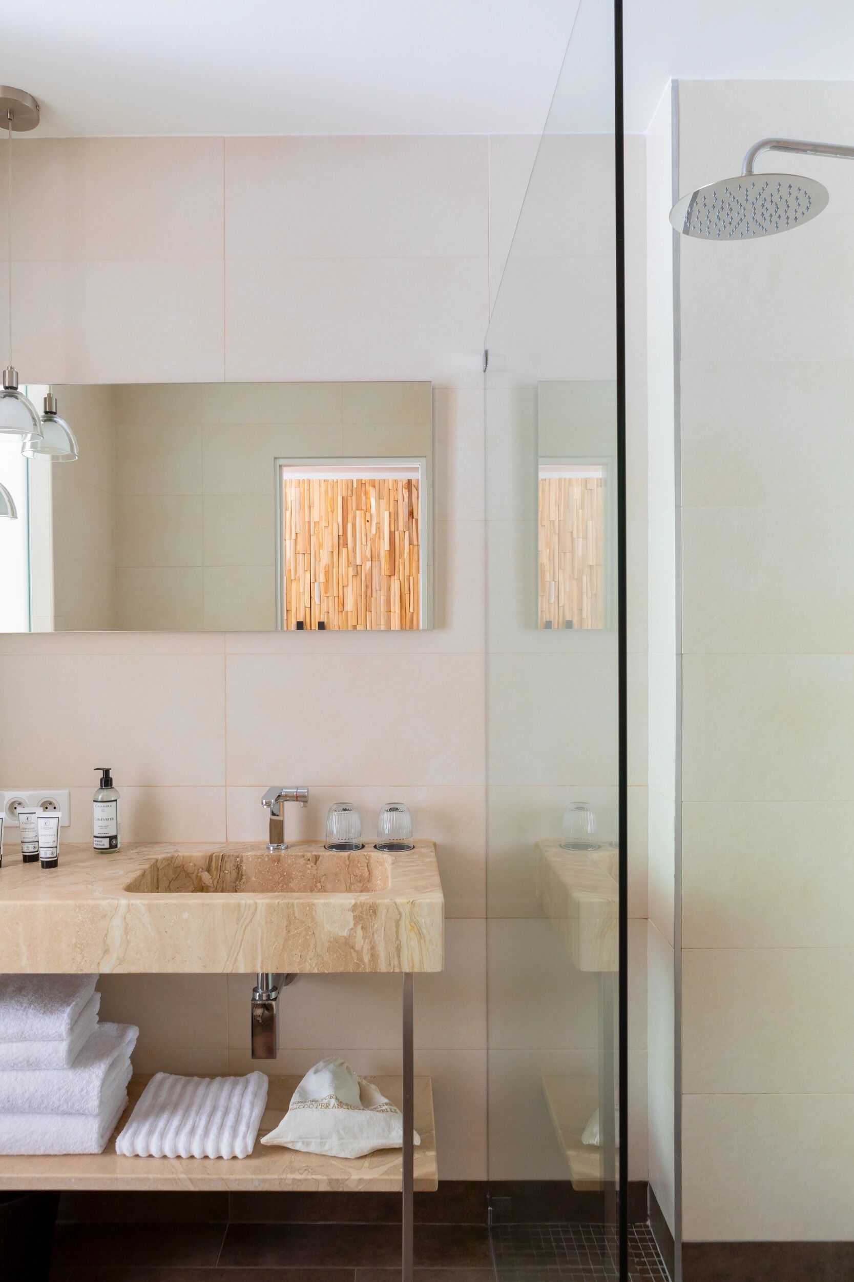 A modern bathroom with a marble sink, a mirror, a wooden panel, and a glass-enclosed shower.