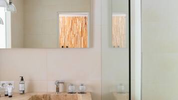 A modern bathroom with a marble sink, a mirror, a wooden panel, and a glass-enclosed shower.