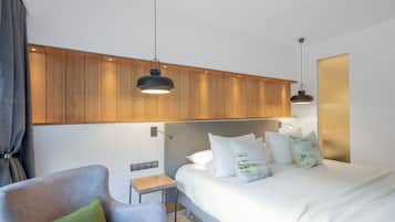 Quarto de hotel moderno com uma cama, uma cadeira, uma mesinha e painéis de madeira na parede.