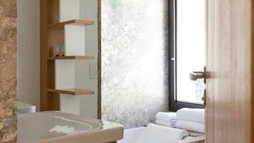 A bathroom with a marble sink, a wooden shelf, a large mirror, and a bathtub with towels.