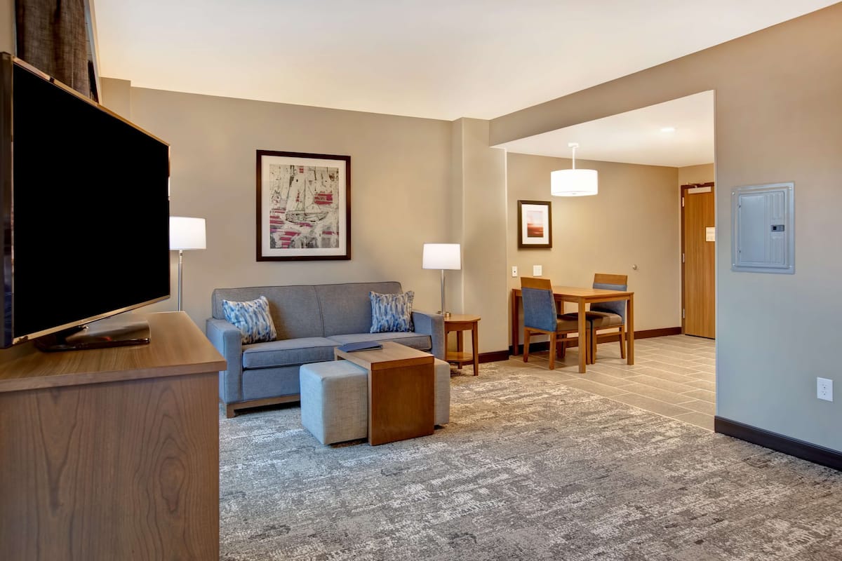 A modern living room with a flat-screen TV, a gray sofa, a coffee table, and a dining area with a table and chairs.