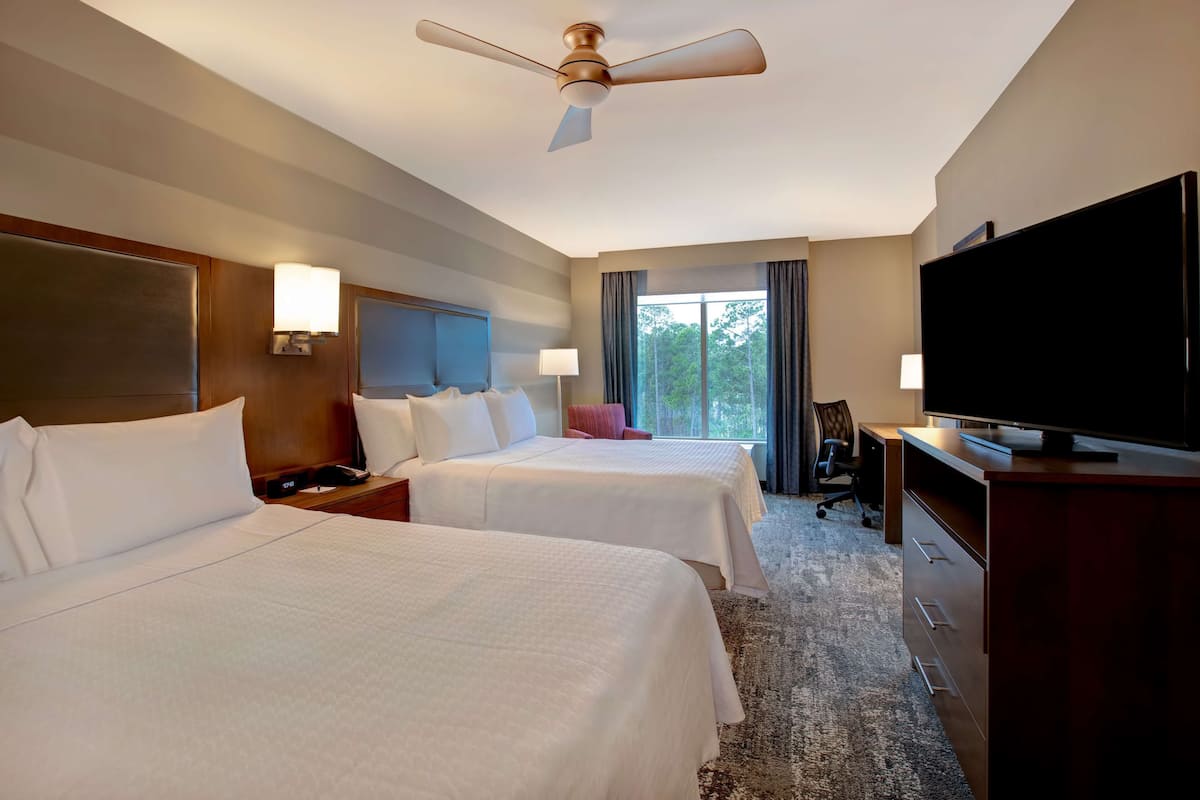 A hotel room with two beds, a television, a desk, and a ceiling fan.