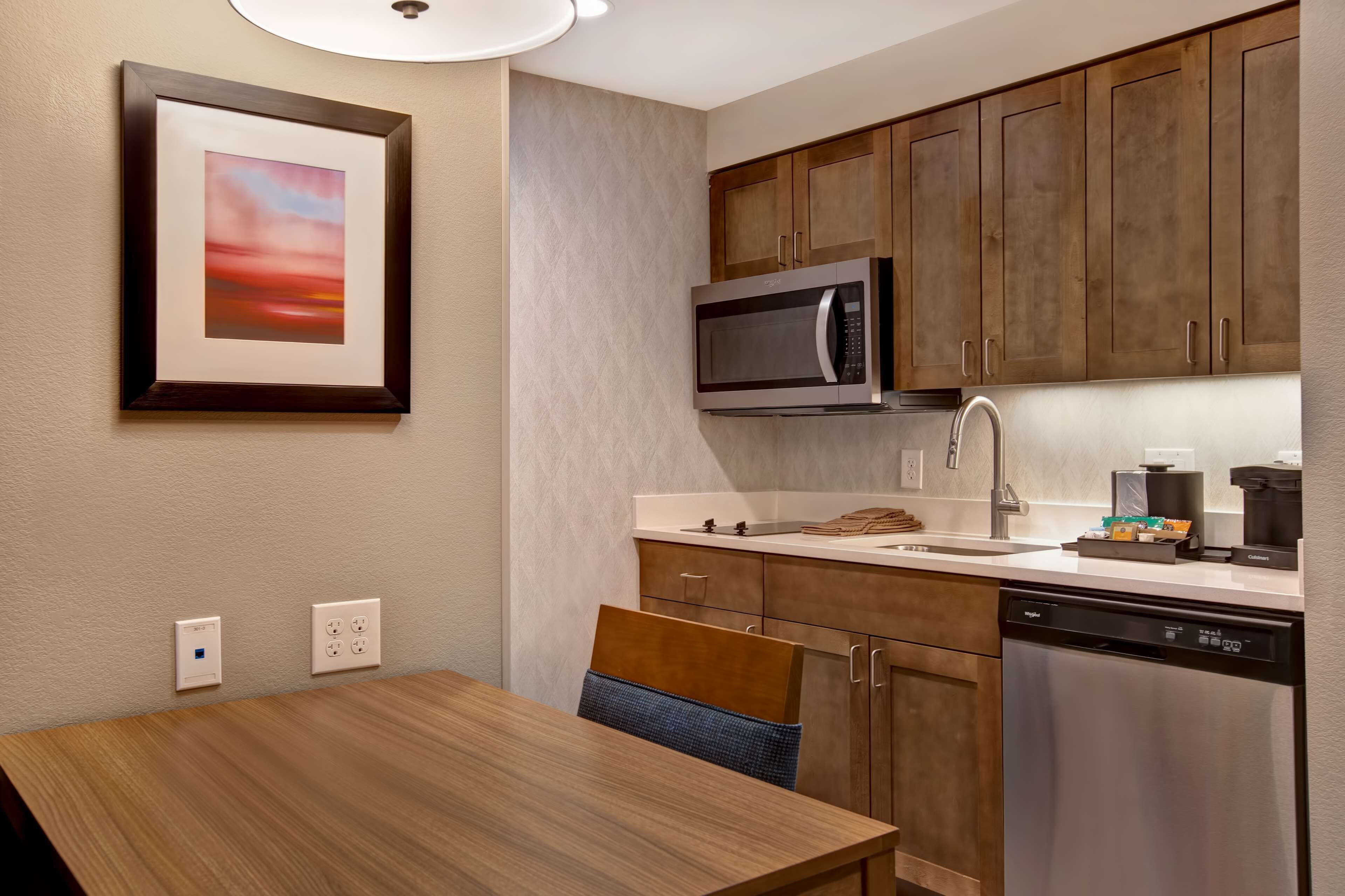 A modern kitchen with wooden cabinets, a built-in microwave, a dishwasher, and a dining area with a table and chairs.