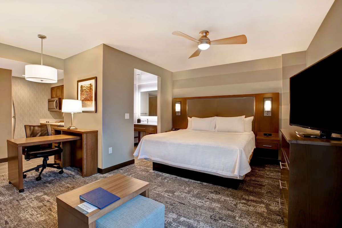 A hotel room with a bed, desk, chair, TV, and a ceiling fan.