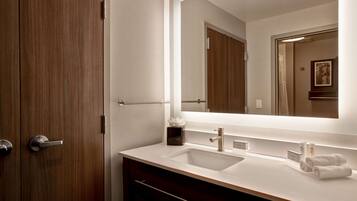 Un baño moderno con puerta de madera, un espejo grande, un lavabo blanco y un perchero para toallas.