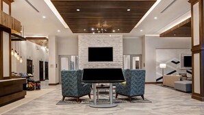Un hall d’entrée spacieux au design moderne, agrémenté d’un mur d’accent en pierre, d’un grand téléviseur à écran plat et de coins salon confortables.