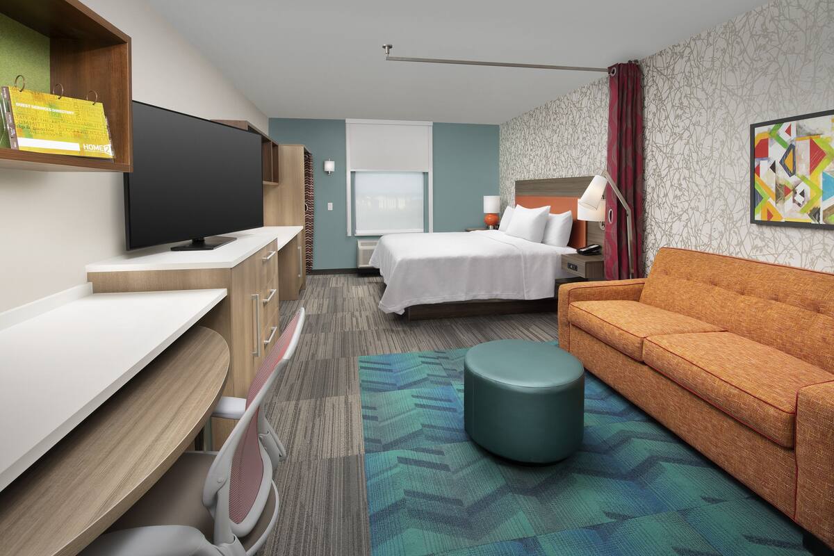A hotel room with a bed, a sofa, a desk, a television, and a window.