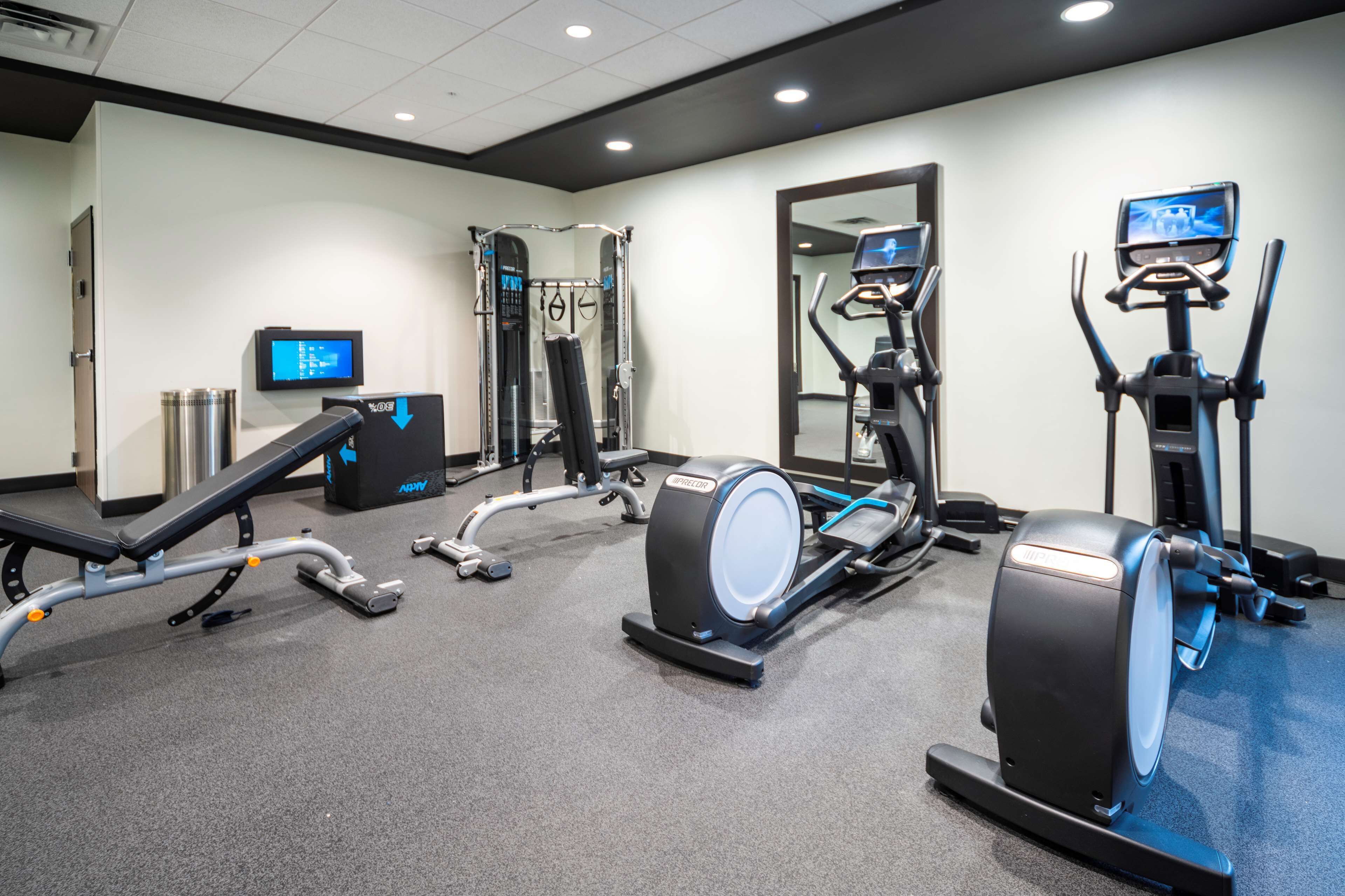 Academia com máquinas de cardio, equipamentos de musculação e uma tela de televisão.